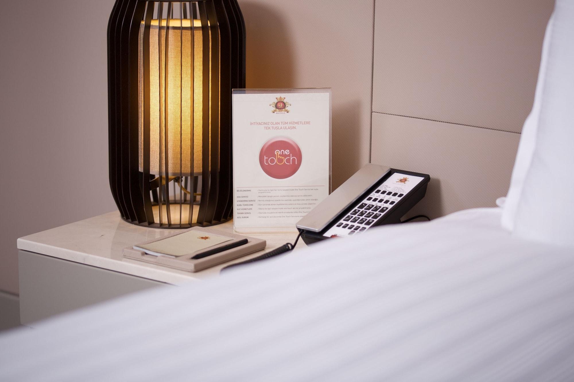 ดอสโซ่ ดอสซี่ โฮเต็ล แอน์ สปา ดาวน์ทาวน์ Hotel อิสตันบูล ภายนอก รูปภาพ The photo shows a bedside setup in a room. There is a stylish lamp with a warm light on a table, alongside a menu or information card that features a logo or brand name. A remote control is also placed on the table, suggesting it might be used for va
