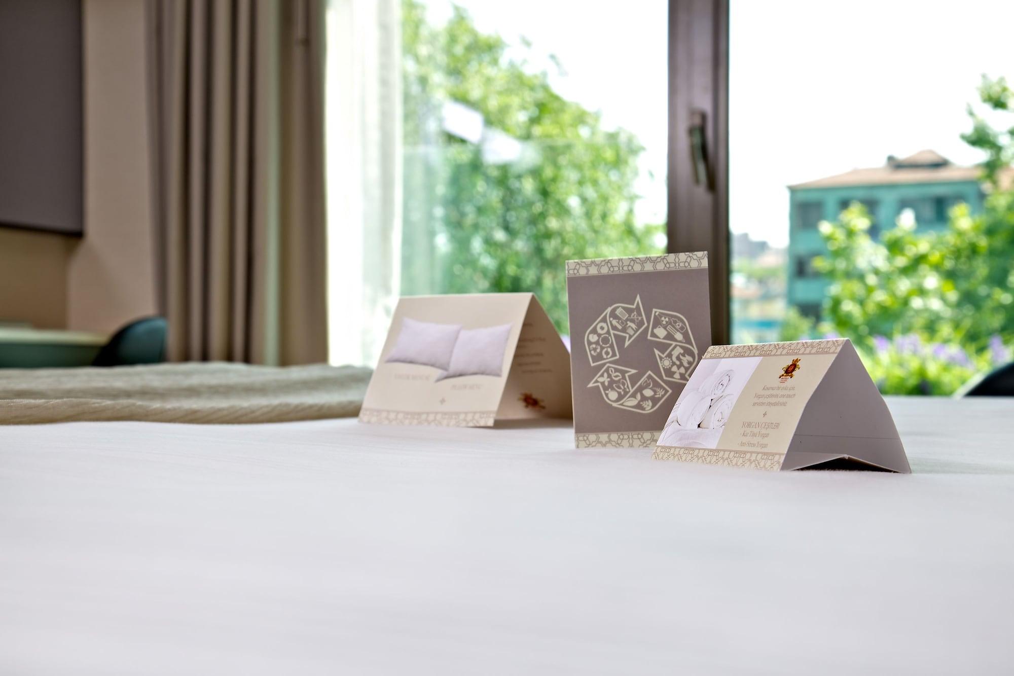 ดอสโซ่ ดอสซี่ โฮเต็ล แอน์ สปา ดาวน์ทาวน์ Hotel อิสตันบูล ภายนอก รูปภาพ The photo shows a neatly made bed with a soft, white bedspread. In the foreground, there are three triangular cards placed upright on the bed. Each card has different designs or text, with one appearing to feature a pillow image and another possibly 