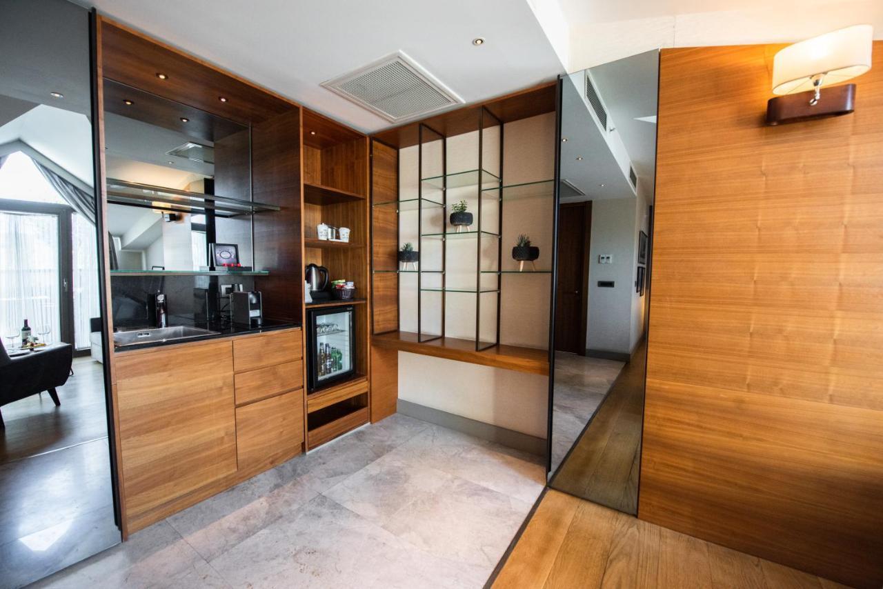 ดอสโซ่ ดอสซี่ โฮเต็ล แอน์ สปา ดาวน์ทาวน์ Hotel อิสตันบูล ภายนอก รูปภาพ The photo shows a modern interior space that features a blend of wood and glass elements. On the left side, there is a kitchenette area with wooden cabinetry and a small refrigerator, while the right side showcases a glass display unit with shelves f