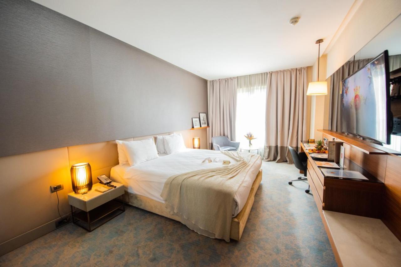 ดอสโซ่ ดอสซี่ โฮเต็ล แอน์ สปา ดาวน์ทาวน์ Hotel อิสตันบูล ภายนอก รูปภาพ The photo shows a modern hotel room with a comfortable layout. There's a large bed with white linens and a soft throw blanket. Beside the bed, there are bedside tables with lamps. A window covered with sheer curtains allows natural light to enter the