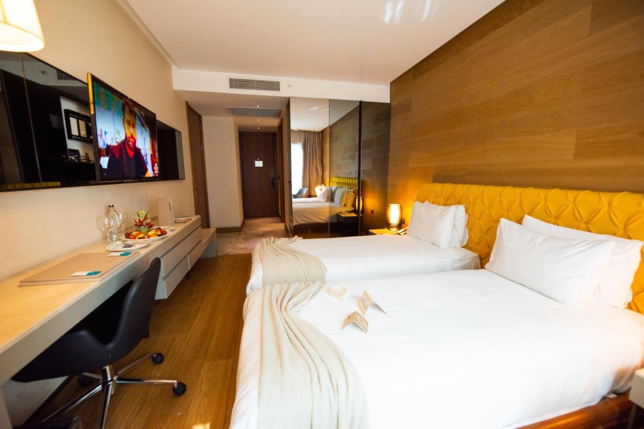 ดอสโซ่ ดอสซี่ โฮเต็ล แอน์ สปา ดาวน์ทาวน์ Hotel อิสตันบูล ภายนอก รูปภาพ The photo shows a modern hotel room featuring two single beds with white linens. There is a stylish yellow accent wall behind the beds. A flat-screen television is mounted on the wall opposite the beds, and a sleek desk and chair are positioned next 