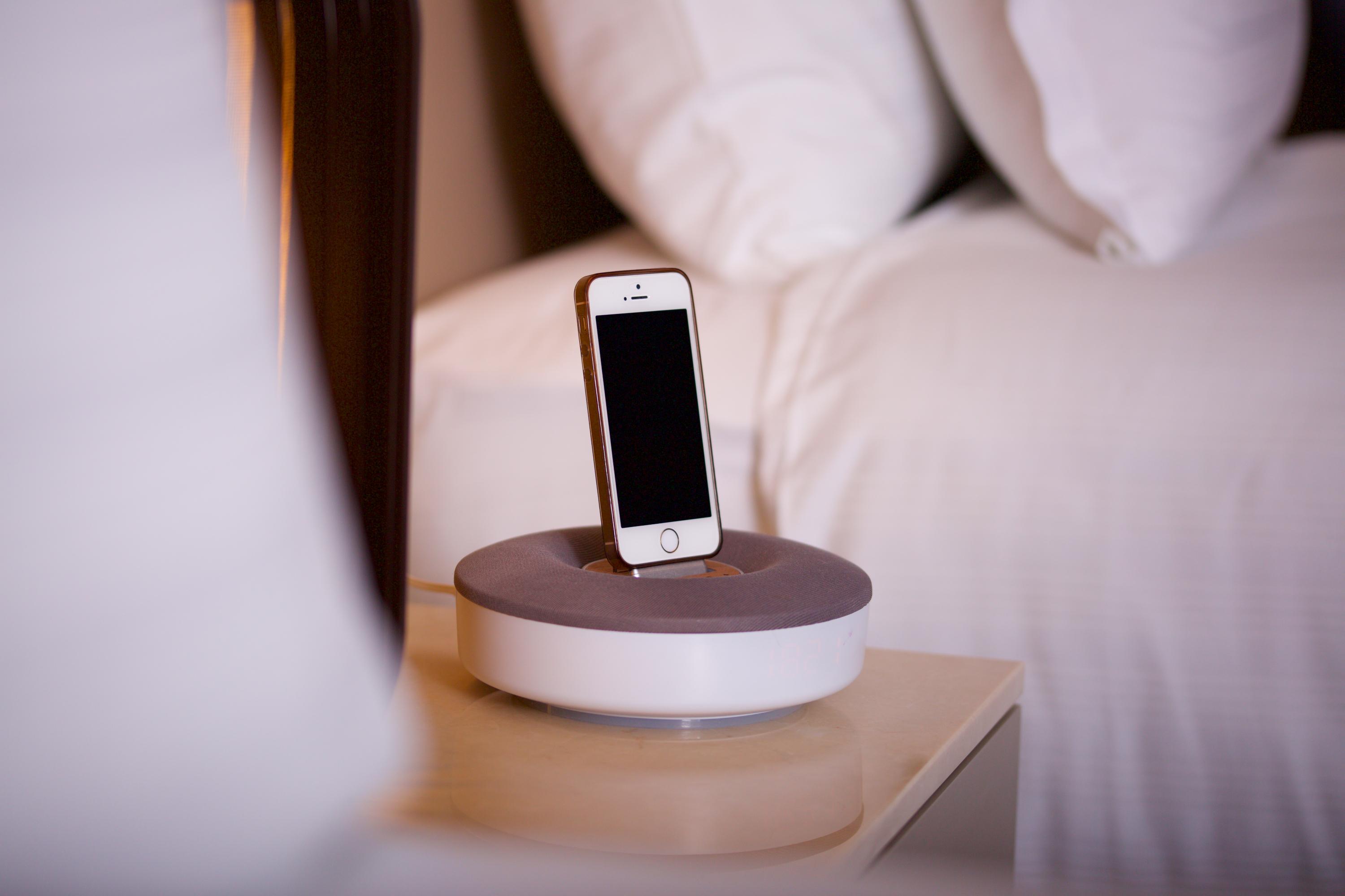 ดอสโซ่ ดอสซี่ โฮเต็ล แอน์ สปา ดาวน์ทาวน์ Hotel อิสตันบูล ภายนอก รูปภาพ The photo shows a smartphone placed on a charging dock. The dock has a circular base with a gray top and a white bottom. The smartphone is upright in the dock, facing forward, and has a blank screen. There are neatly arranged pillows visible in the b