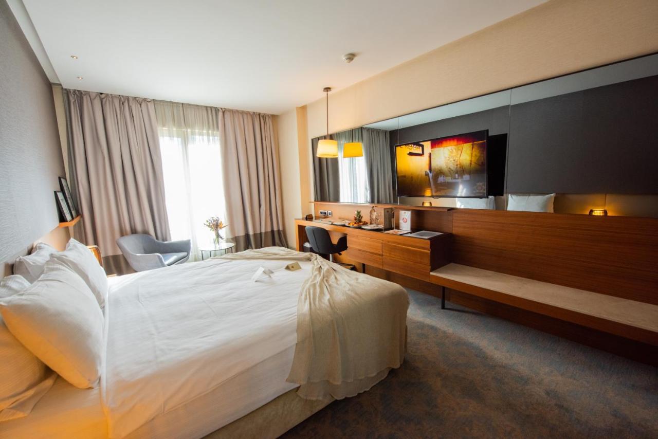 ดอสโซ่ ดอสซี่ โฮเต็ล แอน์ สปา ดาวน์ทาวน์ Hotel อิสตันบูล ภายนอก รูปภาพ The photo shows a modern hotel room featuring a large bed with white linens, set against a soft-toned wall. There is a stylish gray armchair in one corner and a sleek wooden desk with a chair. The room is well-lit, with large windows covered by light
