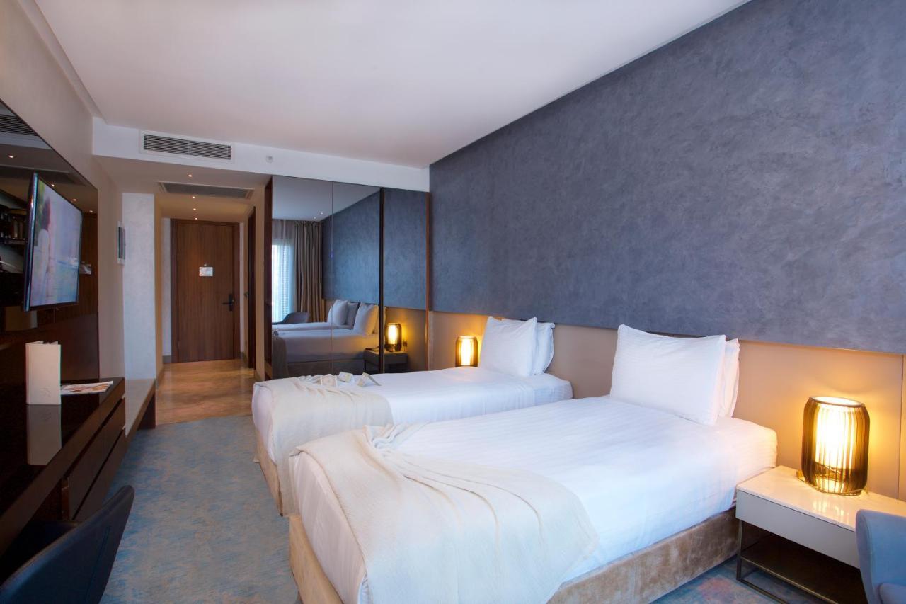 ดอสโซ่ ดอสซี่ โฮเต็ล แอน์ สปา ดาวน์ทาวน์ Hotel อิสตันบูล ภายนอก รูปภาพ The photo shows a modern hotel room featuring two single beds with white bedding. The walls have a stylish gray finish, and there is a decorative element behind the beds. On either side of the beds, there are bedside tables with lamps. A flat-screen 