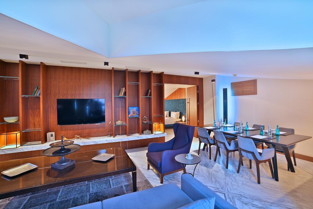 ดอสโซ่ ดอสซี่ โฮเต็ล แอน์ สปา ดาวน์ทาวน์ Hotel อิสตันบูล ภายนอก รูปภาพ The photo shows a modern living space that features an open layout. On the left, there is a comfortable seating area with a sofa and a coffee table. The wall opposite the seating area contains a large flat-screen TV mounted on a stylish wooden panel.